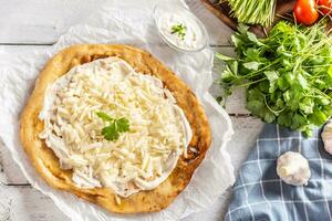Precisely prepared hungarian traditional langos with lovely crust greased with garlic, cream, cheese and herbs, served with vegetables in the backround photo
