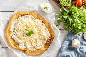 precisamente preparado húngaro tradicional langos con encantador corteza engrasado con ajo, crema, queso y hierbas, servido con vegetales en el fondo foto