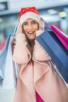 Navidad compras. atractivo contento niña con crédito tarjeta y compras pantalones en Papa Noel sombrero foto