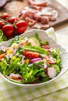 Fresh spring salad with green leaves tomatoes egg radish red onion young peas prosciutto feta cheese and olive oil photo