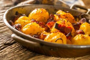 Potatoes. Roasted potatoes with bacon onion and sausages on old oak table photo