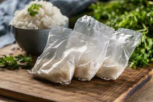 Raw rice in plastic bags on wooden background and cooked rice in bowl photo