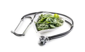 Symbol of healthy heart with stetoscope and heart-shaped bowl full of baby spinach leaves on an isolated white background photo