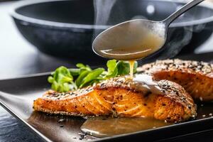 The spoon finishes the portion by pouring a demiglas sauce over the salmon fillets. photo