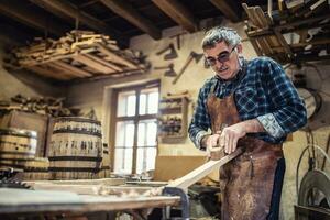 más viejo hombre sofoca el superficie de Tablas de madera antes de utilizando eso a construir de madera barriles foto