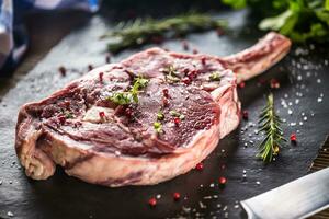 Raw beef tomahawk steak with salt pepper and rosemary on slate plate photo