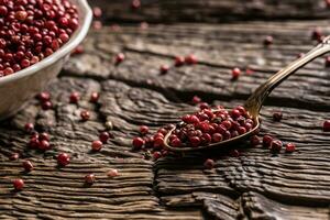 Red peppercorn in bowl and spoon on oak table photo