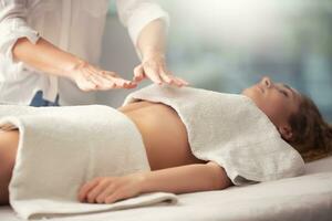 joven niña acostado cubierto con toallas terminado su cofre y cintura recepción reiki energía mediante el manos de un terapeuta foto