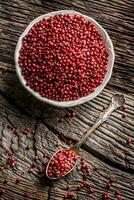 Red peppercorn in bowl and spoon on oak table photo
