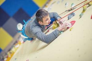 Climber on wall.Young man practicing rock climbing on a rock wall indoors photo