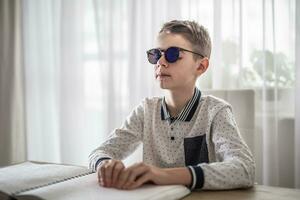 Boy with congenital blindness in dark glasses reads from a book in braille photo