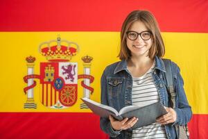 Young female student in glasses hold open textbook in front of flag of Spain photo