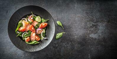 Salmon salad with vegetable in plate on dark kitchen table - Top of view photo