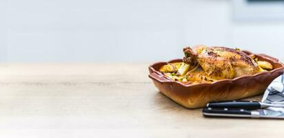Roasted whole chicken with potatoes in baking dish. Tasty food at home on the kitchen counter photo