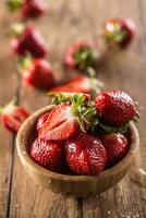 Juicy washed strawberries in wooden bowl on kitchen table photo