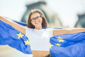 linda contento joven niña con el bandera de el europeo Unión en frente de un histórico edificio algun lado en Europa. foto