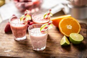 Various fruit smoothies in glass cups with paper straws and wedges of lime and more citruses on the side photo
