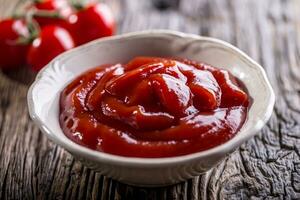 Ketchup or tomato sauce in white bowl and cherry tomatoes on wooden table. photo