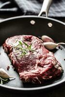 Fresh raw beef Ribe Eye steak in teflon pan with rosemary, garlic, salt and pepper photo