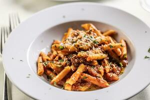 Penne alla arrabiata, typical meal from Italy, served in a nice white plate, decorated with fresh herbs and sprinkled with grated cheese photo