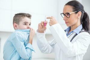 The boy is afraid of injections before preventing vaccination. Young doctor preparing a vaccine for a boy in an ambulance photo