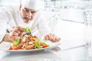 Chef in restaurant kitchen prepares and decorates meal with hands.Cook preparing spaghetti bolognese photo