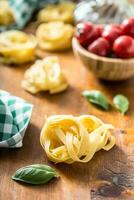 italiano pasta tagliatelle en mesa con albahaca y Tomates foto