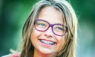 contento sonriente niña con dental tirantes y lentes. joven linda caucásico rubio niña vistiendo dientes tirantes y lentes foto