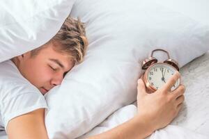 joven hombre con alarma reloj dormido en cama. foto