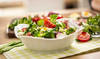 Fresh spring salad with green leaves tomatoes egg radish red onion young peas prosciutto feta cheese and olive oil photo