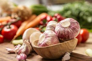 Garlic heads in wooden bowl surrounded by vegetables photo