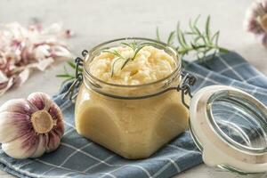 Aromatic garlic paste in a glass jar laid on rustic kitchen cloth with bulbs and peeled cloves and rosemary photo