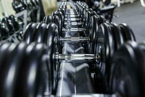 Black dumbbell set. Close up many rubberized dumbbells on rack in sport fitness center , Weight Training Equipment concept photo