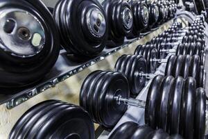 Black dumbbell set. Close up many rubberized dumbbells on rack in sport fitness center , Weight Training Equipment concept photo