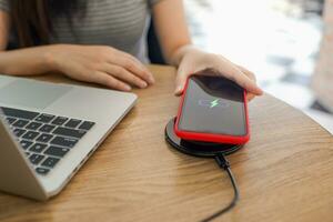 Charging mobile phone battery with wireless device in the table. Smartphone charging on a charging pad. Mobile phone near wireless charger. photo