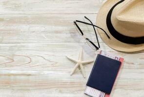 Top view of straw hat, glasses, blue passport and starfish on wooden table. Summer beach and holiday trip concept with copy space. photo