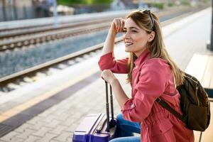 Adult woman is sitting at railway station and waiting for arrival of train. photo