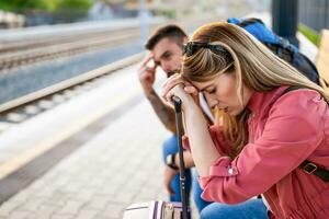 Tired couple sitting at railway station and waiting for arrival of their train. photo
