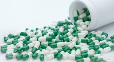 verde y blanco cápsula pastillas derramado fuera de un blanco el plastico botella. farmacéutico industria. prescripción droga. cuidado de la salud y medicamento. farmacia producto. farmacia. cápsula píldora fabricar. foto