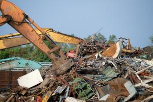 Excavator magnet lifting steel scraps from recycling materials pile at scrap yard in recycling factory. Excavator with electro and magnetic sucker magnet chuck. Special excavator. Scrap metal magnet. photo