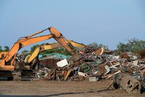 Excavator magnet lifting steel scraps from recycling materials pile at scrap yard in recycling factory. Excavator with electro and magnetic sucker magnet chuck. Special excavator. Scrap metal magnet. photo