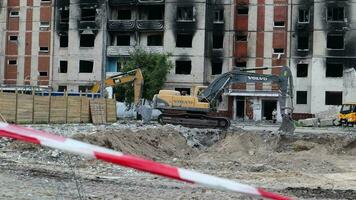 construction travail sur le démolition de à plusieurs étages appartements. clôture fabriqué de rouge et blanc avertissement enregistrer. excavatrice avec hydraulique broyeur à maison démolition. Ukraine, irpin - mai 12, 2023. video