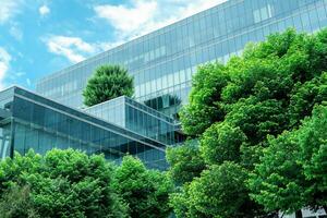 Eco-friendly building in the modern city. Sustainable glass office building with trees for reducing heat and carbon dioxide. Office building with green environment. Corporate building reduce CO2. photo