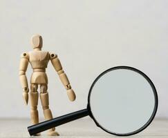 A wooden mannequin holds a plastic magnifying glass on a white background, a concept of information search, problem-solving photo