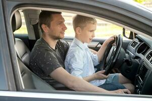 papá da conducción lecciones a un linda chico. sentado detrás el rueda de un coche. sentado en de papá regazo foto