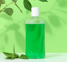Refreshing mouthwash in a transparent plastic bottle on a green background photo