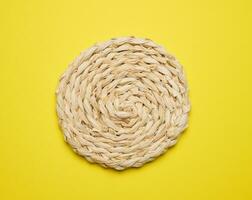 Woven straw coaster for cup, plate, glass for the dining table on a yellow background, top view photo