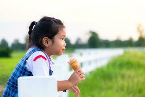 Cute Asian girl in school uniform eating ice cream while on vacation with family, and blured of green field rice  nature background, Happy family concept photo