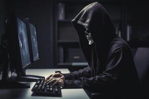 Anonymous skeleton hacker with hood sitting next to computer photo