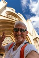 hermoso medio Envejecido hombre visitando Papa Noel maria catedral, tarragona - contento turista tomando un selfie en frente de Iglesia foto